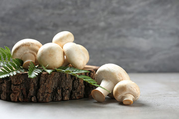 Fresh champignon mushrooms with wooden stump and leaf on table