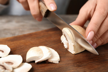 Fototapeta na wymiar Young woman cutting fresh champignon mushrooms on wooden board, closeup view