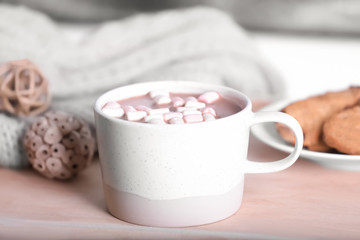 Cup of aromatic cacao with marshmallows on wooden tray near window