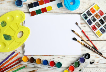Flat lay composition with different paints, brushes and sheet of paper on wooden background. Space...