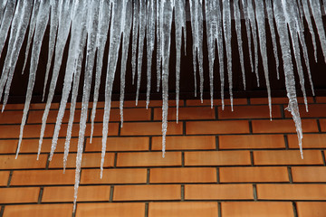 Sharp icicles and melted snow hanging from eaves of roof