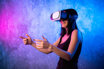 Wondering Young Woman in Virtual Reality Glasses over neon colored background. Shocked Girl wearing VR device. Close-up portrait of Female with VR headset.