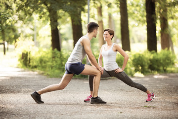 Beautiful happy couple doing together stretching exercises in park