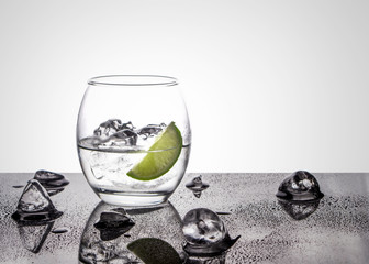 Vodka or Gin with lime in an oval glass on a glossy base with ice cubes against a white back lit background