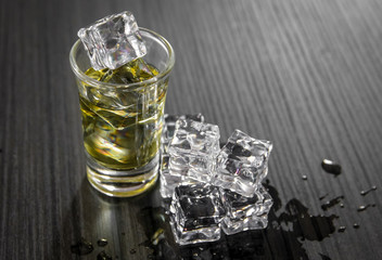 Small glass of strong alcohol drink with ice cubes on black wooden table