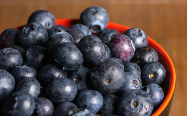 A close up shot of fresh organic blueberries in a red bowl with a wooden background