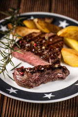 Beef steak with fried potatoes and rosemary in a bowl on a white plate with stars.
