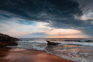 Amazing sunset on the ocean. Waves of the Atlantic ocean on the Guincho beach. Dramatic cloudy sky and reflection of the sunlight on water. Atlantic coast.Lisbon.Sintra-Cascais natural park. Portugal.