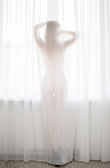 slim girl standing in room behind white curtain