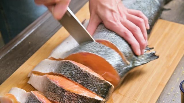 Close-up of female hands are cutting with a knife a large salmon on a wooden table of home cooking