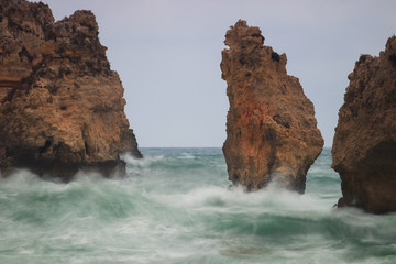 Rocks and pillars in the ocean at Lagos, Algarve, Portugal during high waves and wind. Showing...