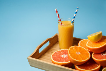 cut in half juicy citruses on a blue background on a tray next to a glass of fresh tasty juice