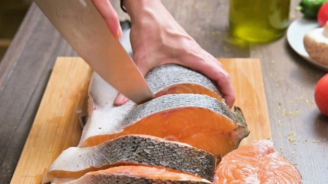 Close-up of female hands are cutting with a knife a large salmon on a wooden table of home cooking