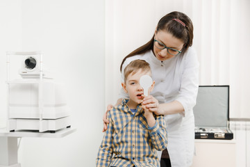 Small cute blonde boy covers eye with spatula to check his vision, opening mouth, squinting second