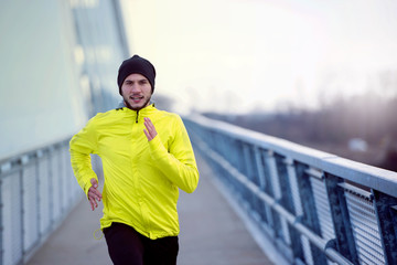 Attractive fit man running fast along big modern bridge. Exercising, Jogging, Sport, Winter. Male athlete running.