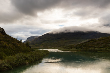 Mountain with cloud on top above the lapplander village of Alesjaure in northern Sweden as seen while walking the Kungsleden (Kings trail) hike in late summer an early morning before after sunrise. 