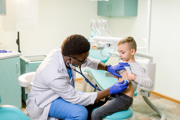 Obraz premium African American Doctor examining child by stethoscope. Happy child boy at the doctor's consultation in hospital. Medical exam at clinic by pediatrician. Pediatric, healthcare and people concept.