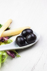 DETALLE DE ACEITUNAS NEGRAS EN CUCHARA BLANCA DE PORCELANA