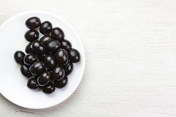 PLATO DE ACEITUNAS NEGRAS SOBRE MESA DE MADERA CLARA
