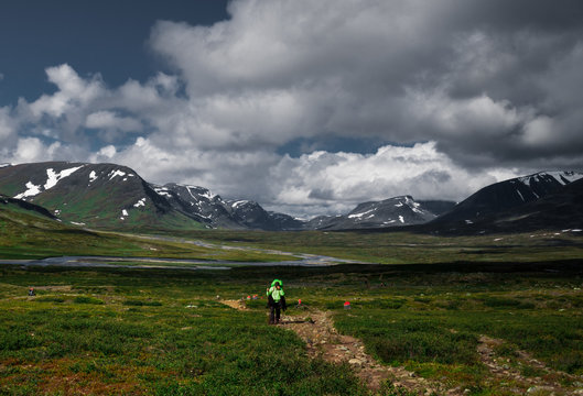 Person walking on a trail leading away from a river below mountains in a valley along the Kungsleden (Kings trail) hike in northern Sweden. Summer and open space creating a feeling of freedom. 