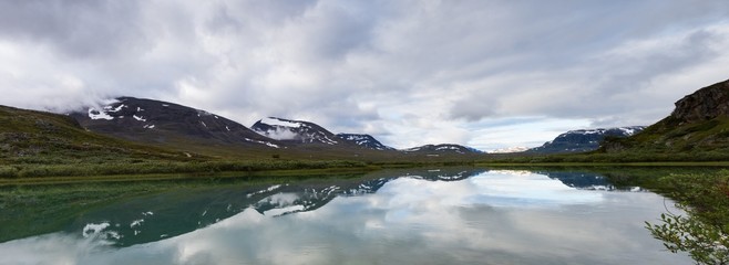 Panorama of Alesjaure lake with mountains behind creating refletioctions just before sunrise. Captured while walking Kungsleden (Kings path) in northern Sweden. Just outside Alesjaure cabin.