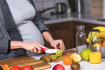 Beautiful smiling young pregnant woman preparing healthy food with lots of fruit and vegetables at...
