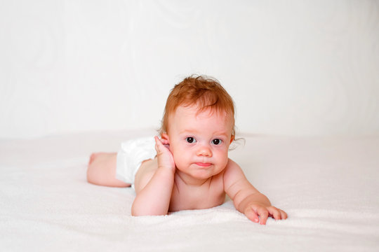 Portrait of cute redhead infant baby in diaper in light bedroom. Family, motherhood, love, health, innocence and care