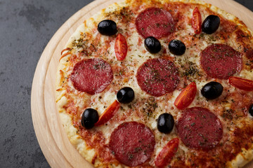 Pizza with salami, mozzarella cheese, cherry tomatoes, black olives and oregano. Home made food. Concept for a tasty and hearty meal. Black stone background. Copy space