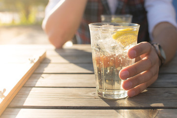 A glass of sparkling water and lemon on a wooden table held by a hand