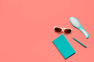 Trendy colorful flat lay composition. Coral colored desk with turquoise diary, hair comb, white glasses and pen. Minimalistic living coral toned image for bloggers, designers, magazines etc.