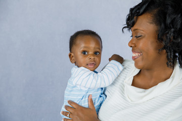 Beautiful African Amercian Woman wHolding Her Baby boy on a Gray Background