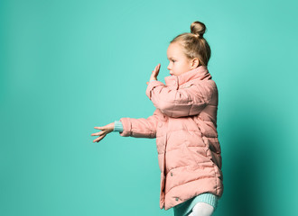Cute little girl in a spring coat points with two palms of her hands to the side to free space.