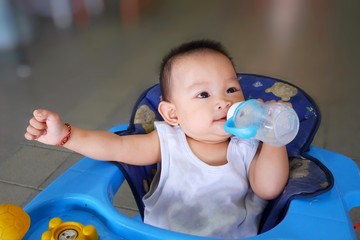 Asian baby drinking water and milk from baby milk bottle by herself. She sitting in a baby chair. 