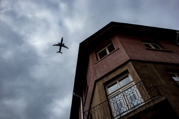 Airplane silhouette on the blue-white background of the cloudy autumn evening sky and two-stories house with small empty balcony in Sofia, Bulgaria