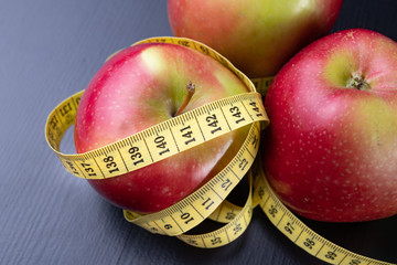 Tasty, ripe apples wrapped in a measuring tape. Fruit on a dark table.
