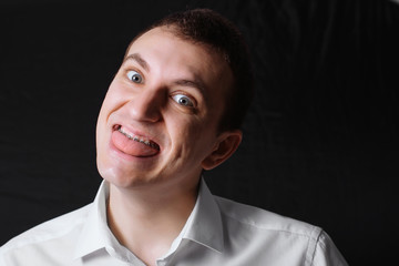 Obraz premium Portrait of a man of Caucasian appearance in orthodontic braces, metal brackets on his teeth in a white shirt on a black background. Dental concept, medicinal alignment of teeth orthodontist.