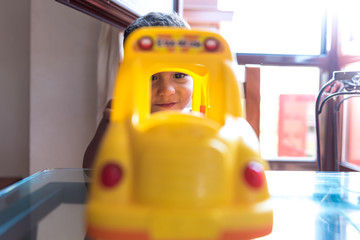 Child boy playing with a school bus toy indoors.