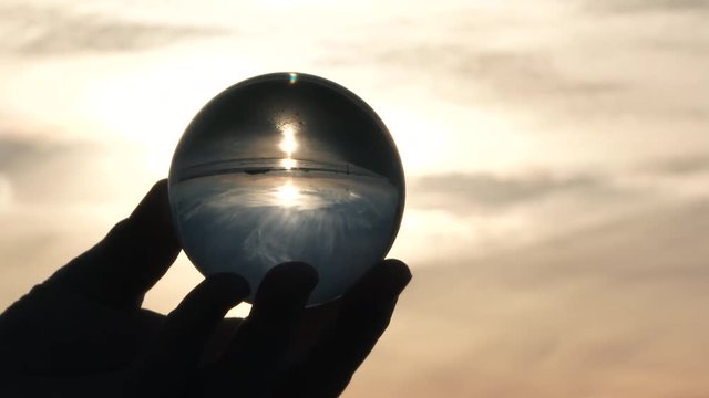 Person holding glass crystal ball showing reflection of sunset at the beach.