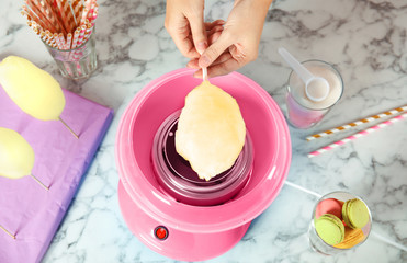 Woman making cotton candy using modern machine at table, top view