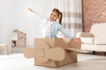 Cute little girl playing with cardboard airplane in living room