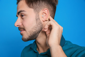 Obraz premium Young man adjusting hearing aid on color background