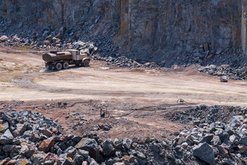 The tank truck wets water the surface of the road in a quarry open pit mining of granite stone. Process production stone and gravel. Quarry mining equipment.
