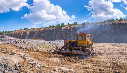 A large tracked bulldozer in a quarry open pit mining of granite stone. Process production stone and gravel. Quarry mining equipment.