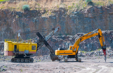 A large tracked excavator and pneumatic hammer in a quarry open pit mining of granite stone. Process production stone and gravel. Quarry mining equipment.