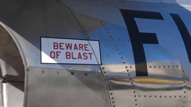 Tilt down to BEWARE of BLAST near engine of 1950s fighter jet. F-86 Sabre. Handheld shot with stabilized camera.
