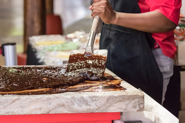 Closeup of an artisan chocolate worker mixing melting chocolate with spatulas on a table.