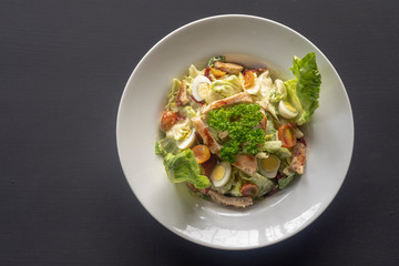 Caesar salad on a white plate on a dark background.