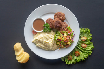 meat patties with sauce, mashed potatoes and salad on a white plate on a dark background, mashed...
