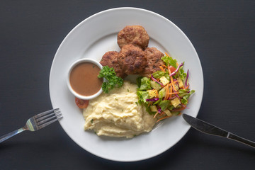 meat patties with sauce, mashed potatoes and salad on a white plate on a dark background, mashed potatoes and salad on a white plate on a dark background