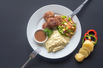 meat patties with sauce, mashed potatoes and salad on a white plate on a dark background, mashed potatoes and salad on a white plate on a dark background